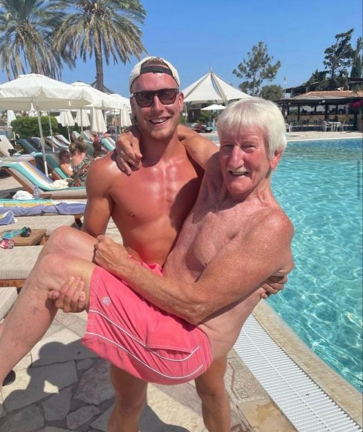 A young man carrying an older man next to a swimming pool.