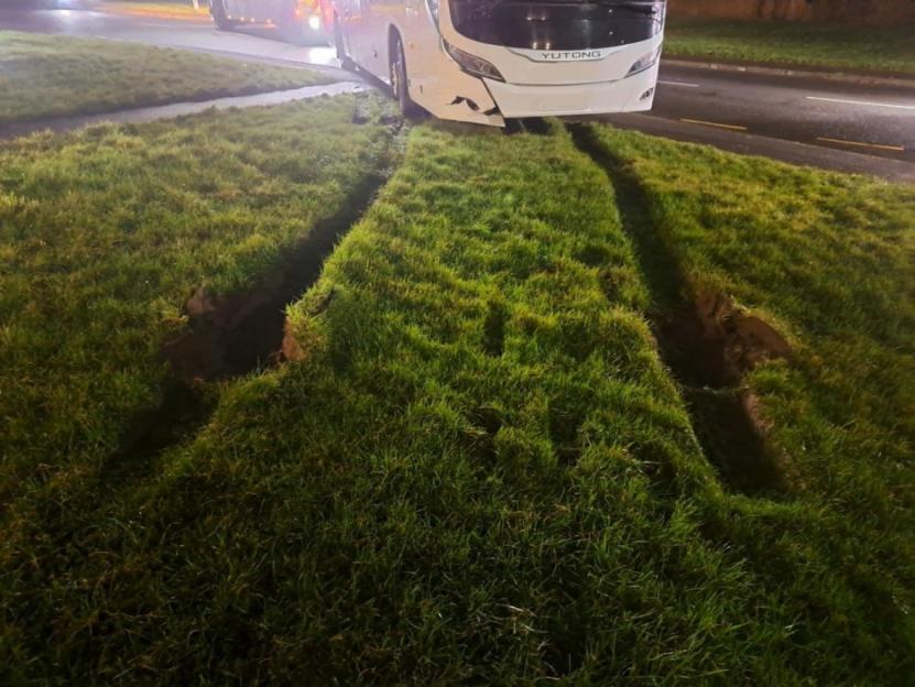 Bus stuck in a muddy ditch, with visible tire tracks in the grass.