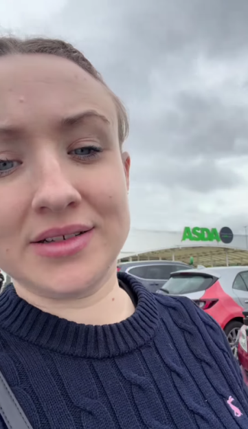 Woman in a navy blue sweater in front of an ASDA sign.