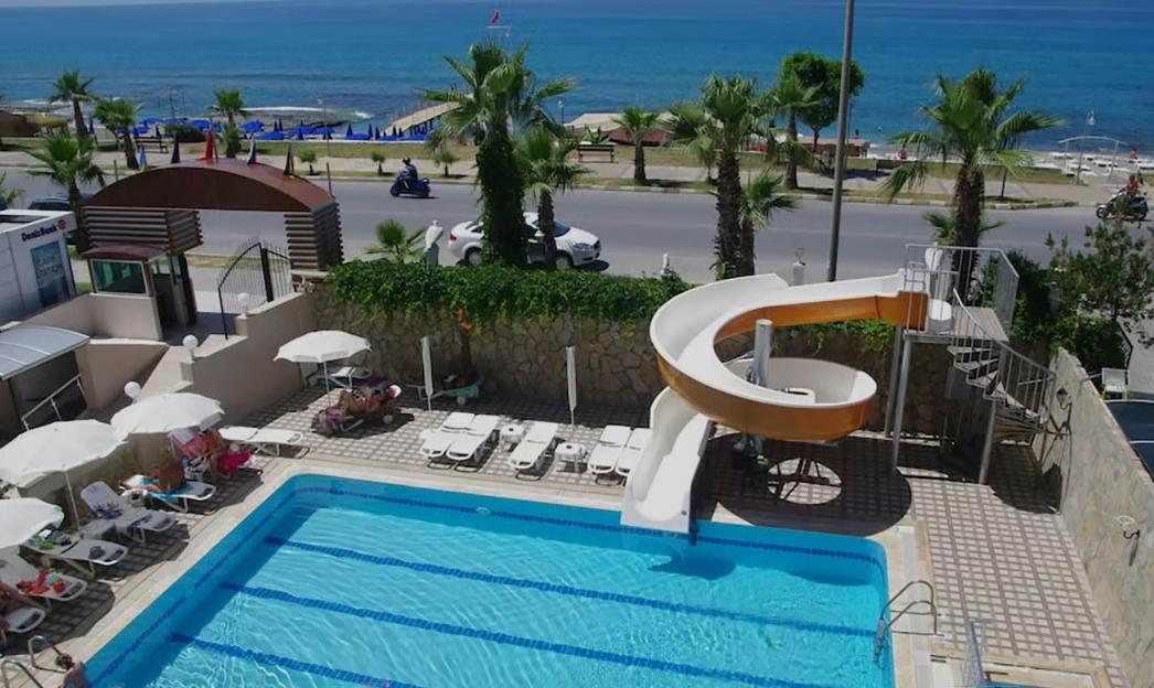 A hotel pool area with a water slide, lounge chairs, and a view of the sea and road in the background.