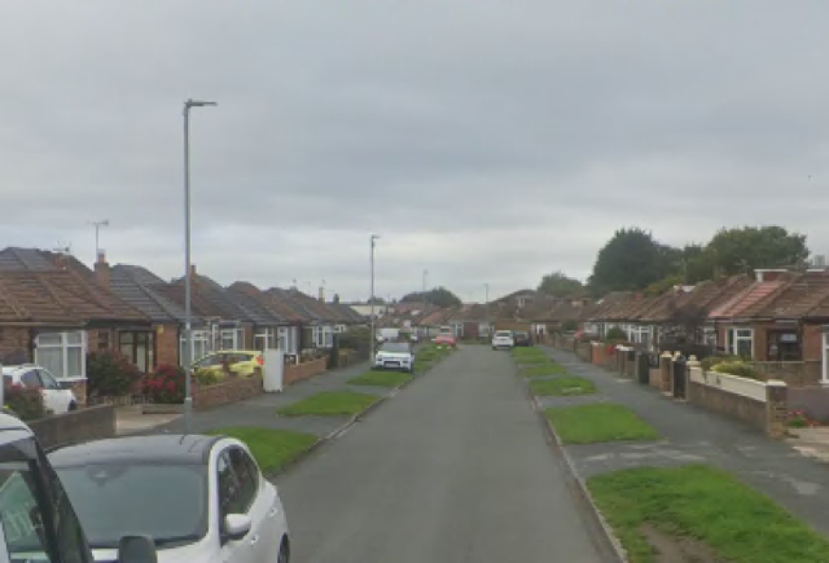 Street view of a residential neighborhood with bungalows lining both sides of the road under a cloudy sky.