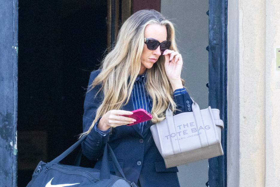 Michaela Crawford, a former prison officer, adjusts her sunglasses while holding a phone and two bags.