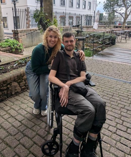 Tom Davies in a wheelchair with his girlfriend Alex Ross.