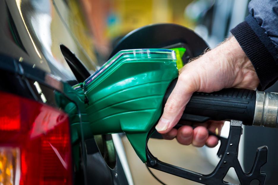A person's hand holding a green fuel pump nozzle in a car's gas tank.