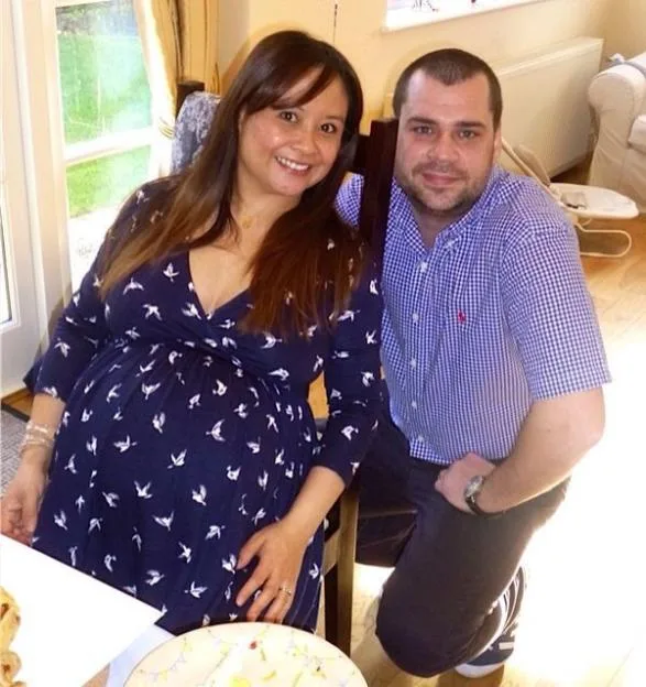 A pregnant woman in a navy dress and a man in a blue plaid shirt smiling at the camera.