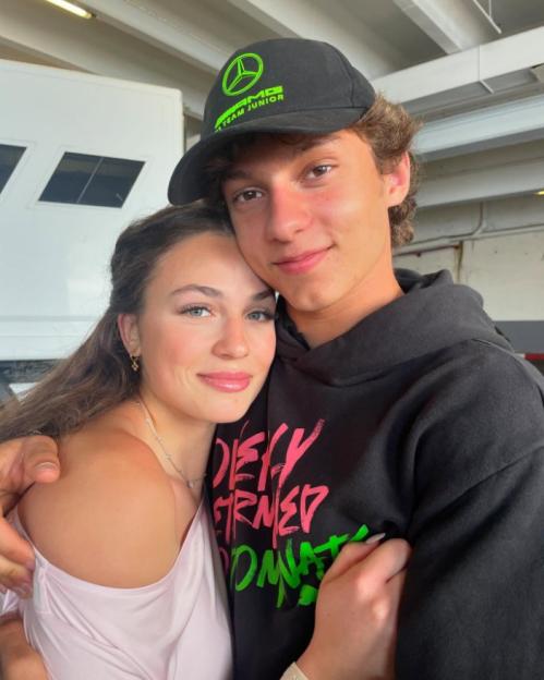 A young man in a black Mercedes AMG cap and a young woman in a pink top embracing.
