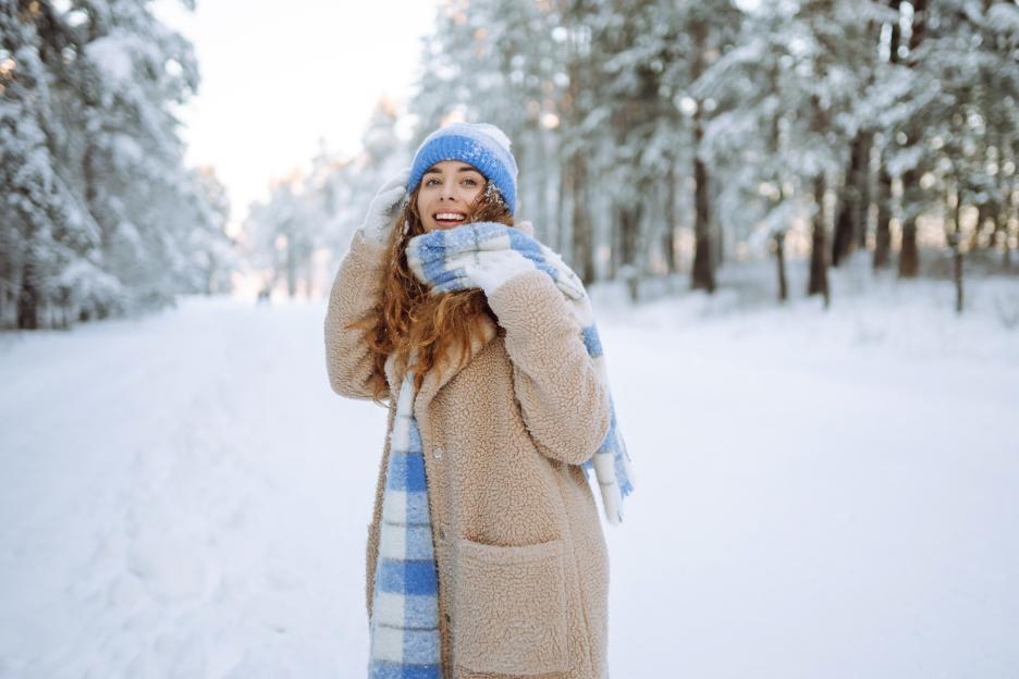 Smiling woman in a snowy park, wearing a blue and white scarf and hat.