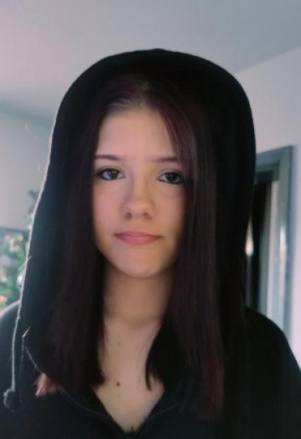 A young woman with dark hair and a black hoodie stares at the camera.