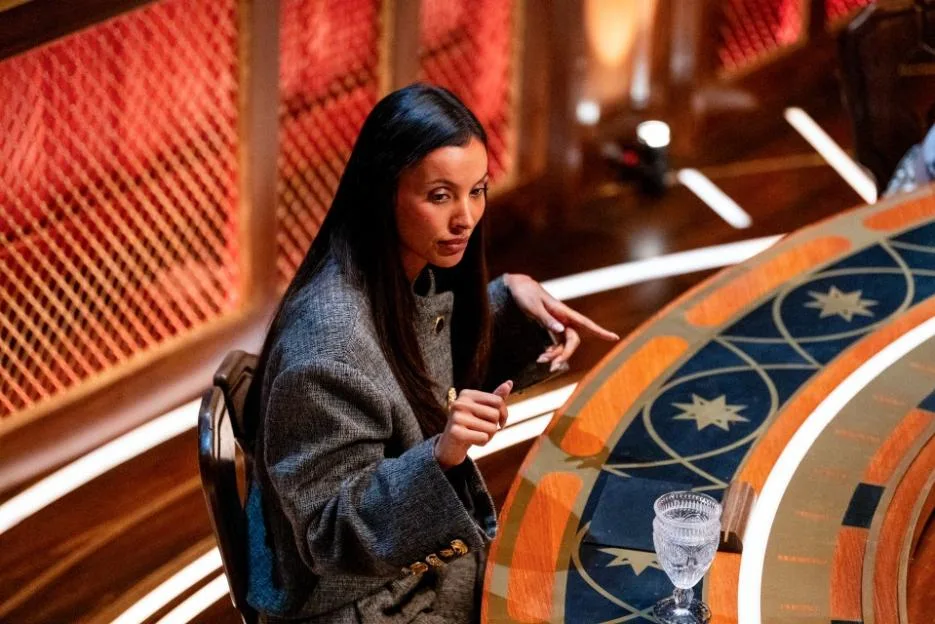 Maya Jama sitting at a round wooden table in The Traitors.