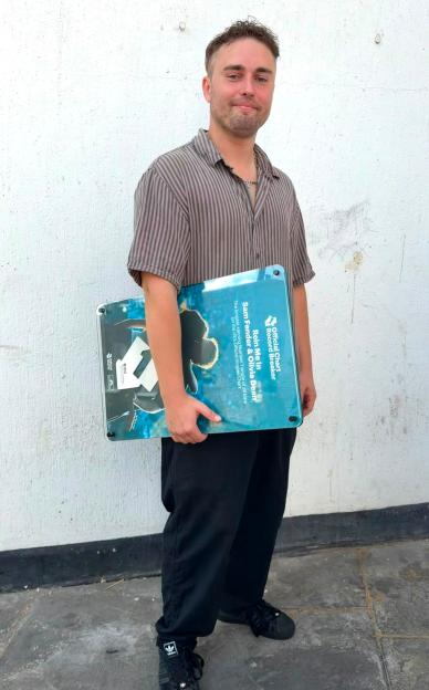 A young man holding a record breaker award for the song "Rein Me In" by Sam Fender & Olivia Dean.