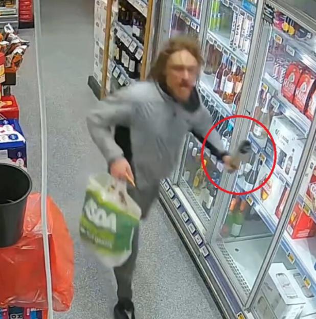 A man in a grey sweatshirt wielding a bottle of wine at staff in a store.