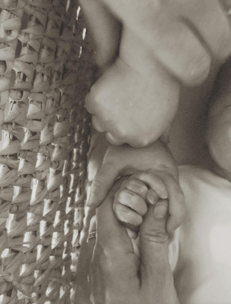 A baby's hand grasping an adult's thumb, with a woven basket on the left.
