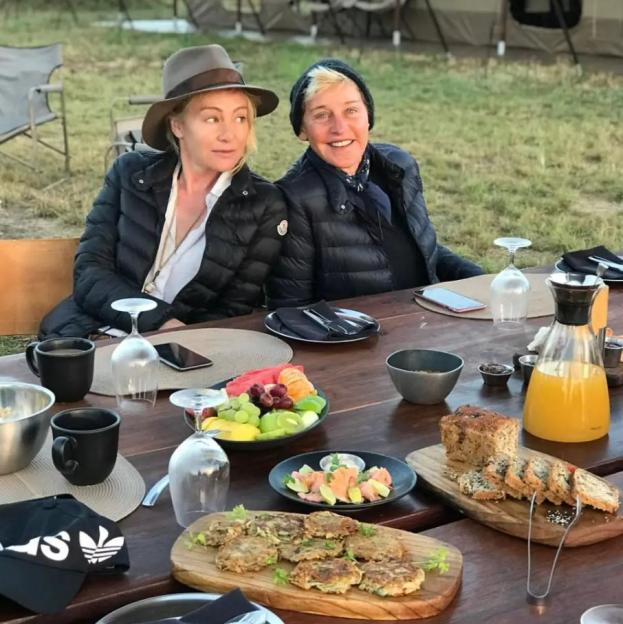 Ellen DeGeneres and Portia de Rossi sitting at a table with food and drinks.