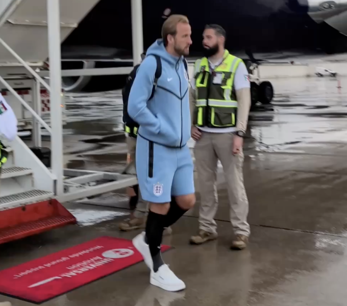Harry Kane walking on an airfield next to a person in a safety vest.