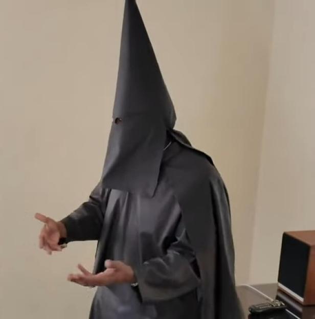 Kanye West wearing a black KKK-style hood and robe, talking to DJ Akademiks.