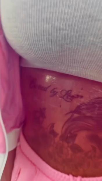 The torso of a person with a tattoo on their stomach that reads "Owned by Logan."