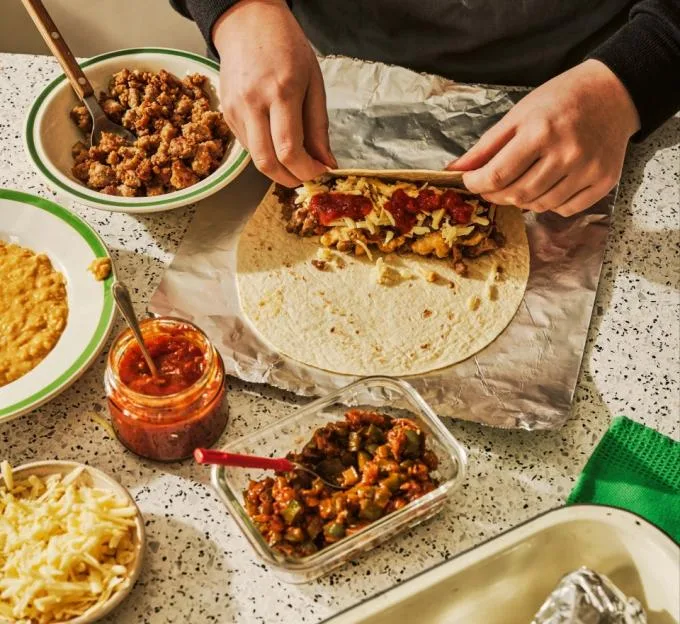 Hands rolling a breakfast burrito with sausage, cheese, and salsa on a tortilla.