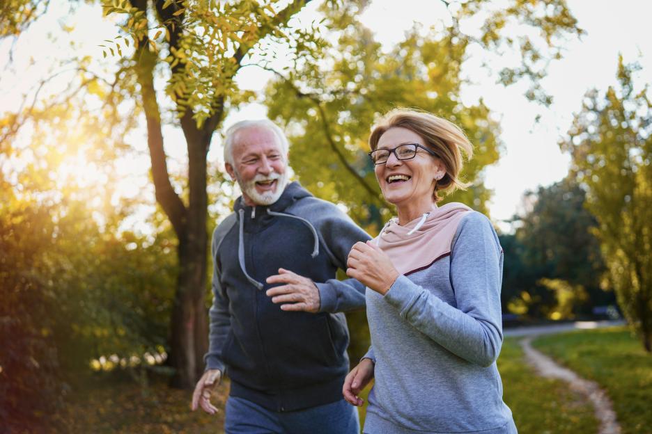 Two joyful senior adults jogging in a park on a sunny day.