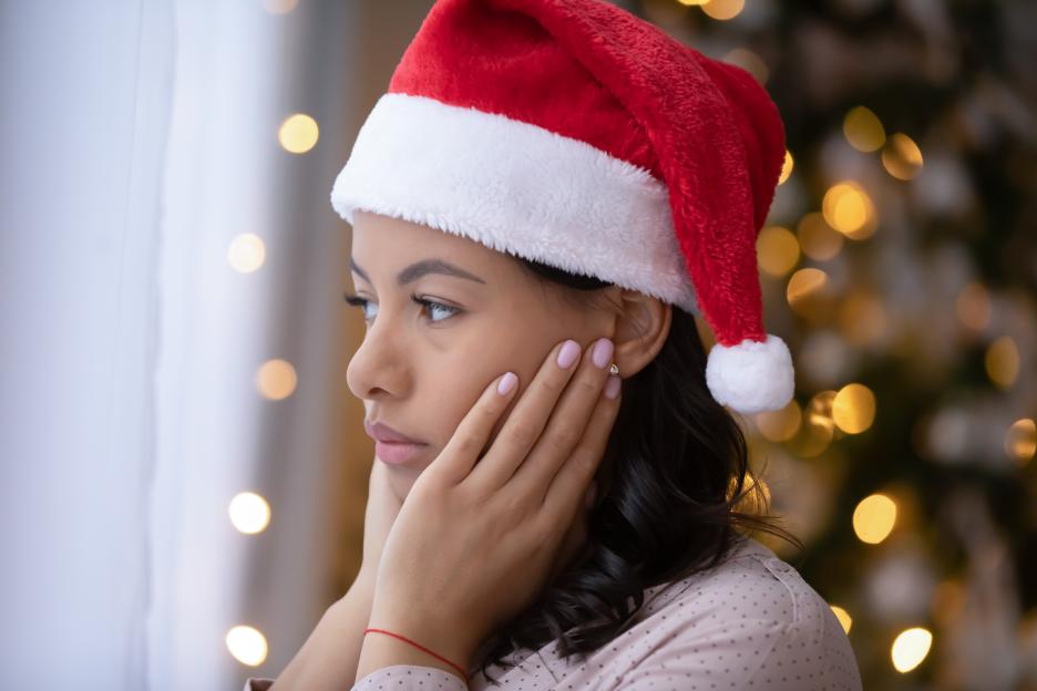 Upset African American woman wearing a Santa hat, looking into the distance with her hands on her cheeks, symbolizing loneliness during Christmas.
