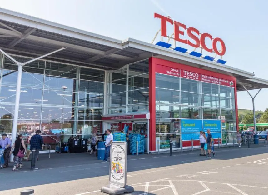 Shoppers walking near the entrance of a Tesco supermarket.