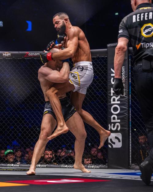 Two MMA fighters grappling in an octagon, with one fighter holding the other in a standing chokehold.