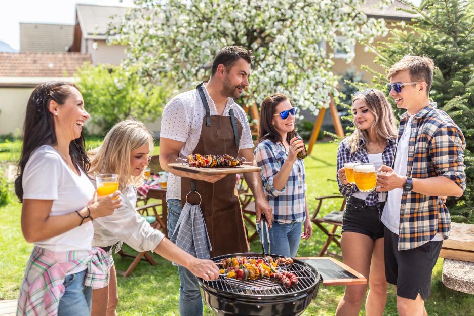 A group of friends laughing and drinking while grilling food outdoors.