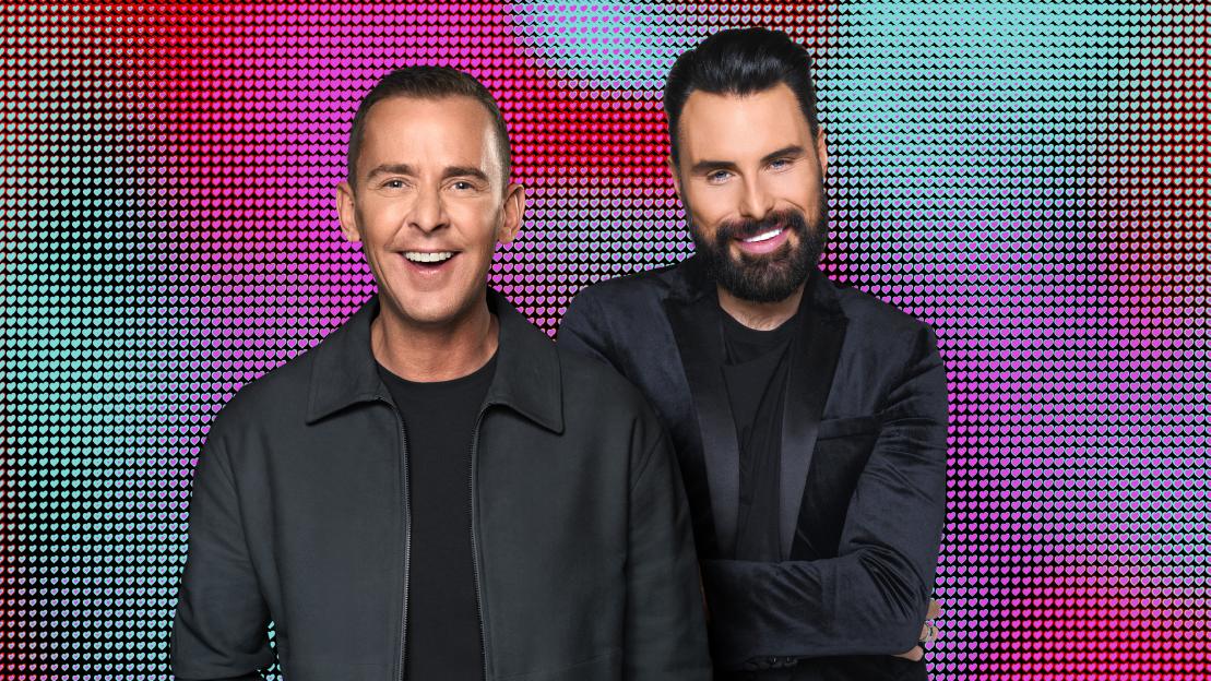 Scott Mills and Rylan standing against a background of small, multicolored hearts.