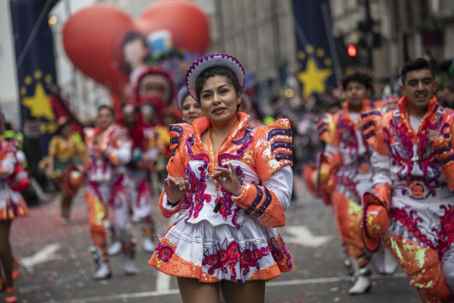 A woman in an orange, purple, and white sequined costume and hat performs in a parade.