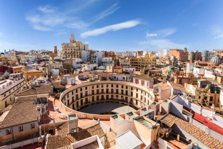 Scenic view of Valencia city featuring a circular building surrounded by traditional rooftops under a blue sky.