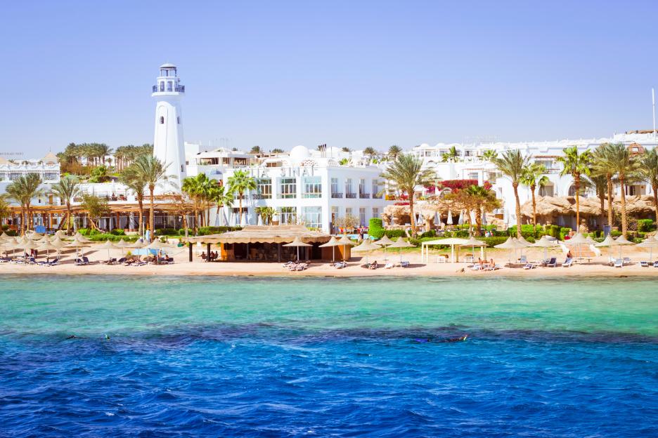 Coastal lighthouse and hotel with palm trees on a beach in Sharm El Sheikh, Egypt.