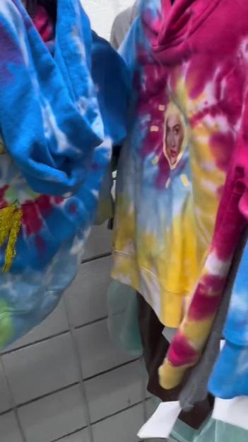 Tie-dye hoodies on a rack, one with a face printed on it.