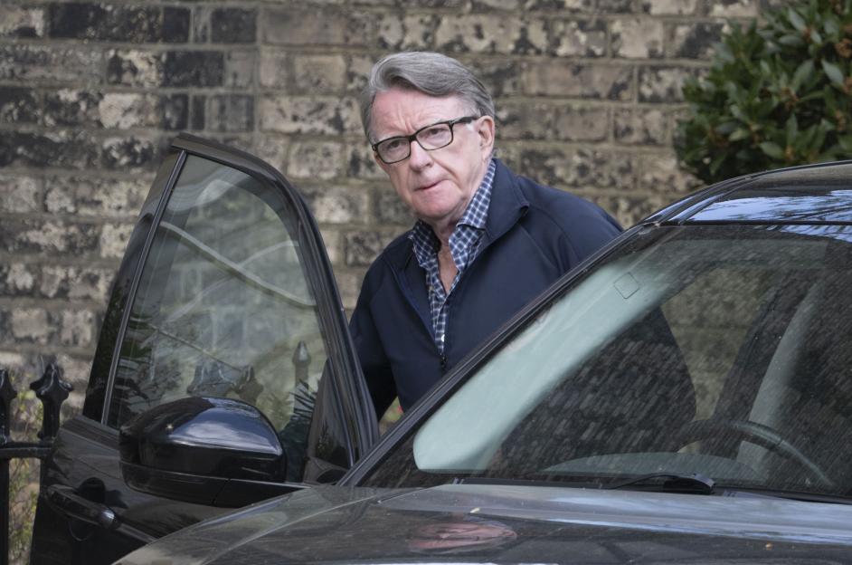 Peter Mandelson emerging from a car in front of a brick building.