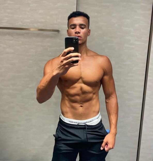 A muscular man in athletic shorts and Calvin Klein underwear takes a mirror selfie with his phone.