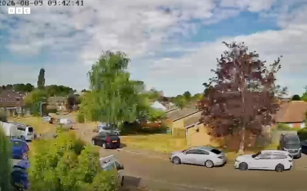 Video still showing a residential street with cars parked and houses visible, captured moments before a gas explosion.