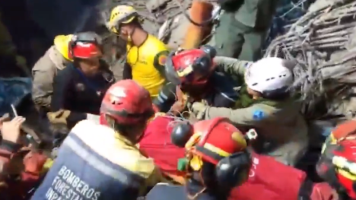 Rescue workers in helmets and uniforms digging through rubble.