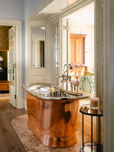 A luxurious copper bathtub with silver accents and an antique faucet, with several doorways leading to other rooms.