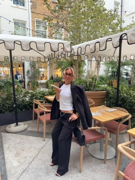 Yasmin Hadlow posing in an outdoor courtyard while holding a phone.