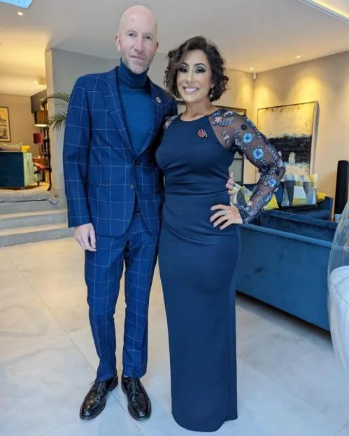 Saira Khan with a man, both wearing blue outfits and poppy pins.