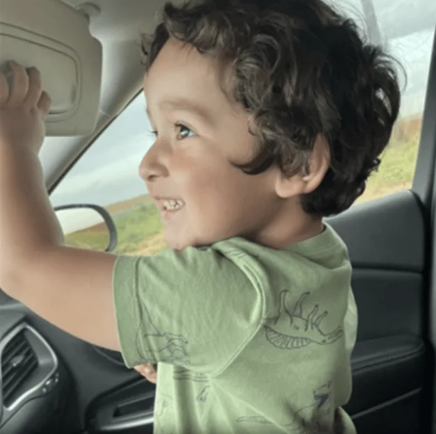 Wyatt in a car, smiling and looking out the window, with his hand on the sun visor.