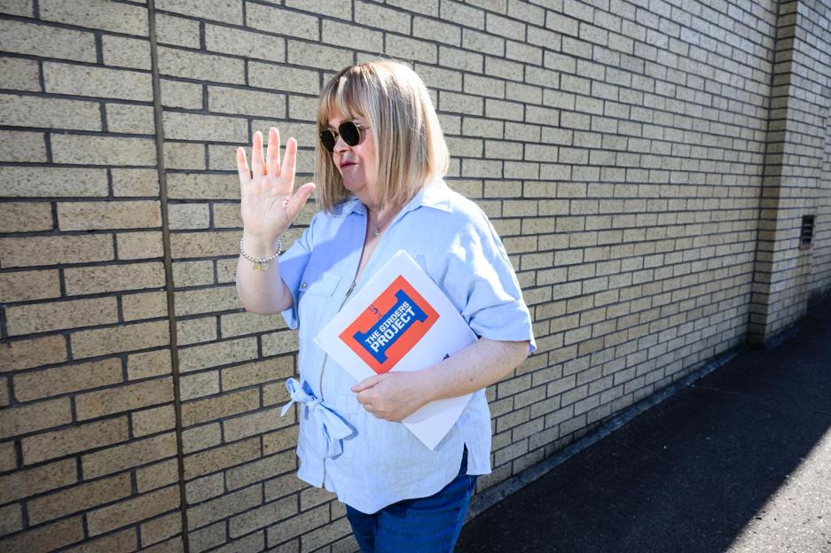 Susan Boyle waving while holding a folder labeled "The Girders Project."