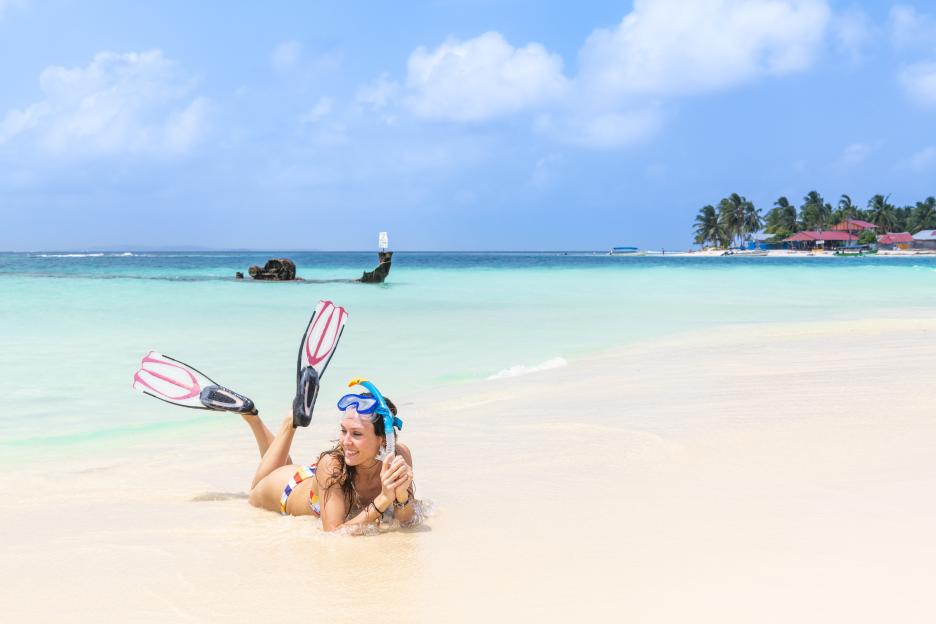 A woman in a bikini with snorkeling equipment lying on a tropical beach.