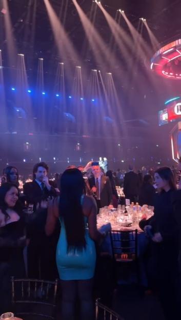 A large gathering of people socializing in a dimly lit event space with spotlights.