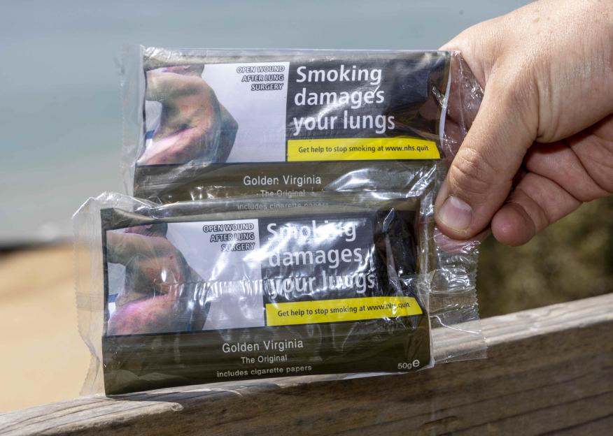 A hand holding two packets of Golden Virginia rolling tobacco, both showing graphic health warnings.