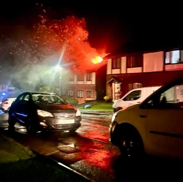 A house fire with flames erupting from the roof at night.