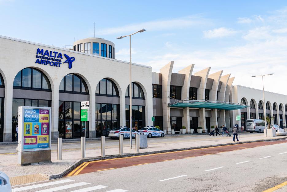 Malta International Airport exterior with police cars and travelers.