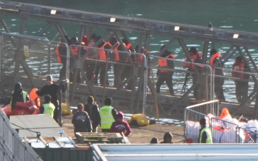 Individuals wearing orange life vests disembark from a Border Force vessel at a facility in Dover, Kent.