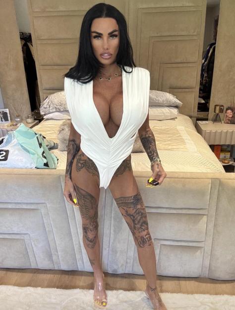 Katie Price poses in a white outfit in a bedroom setting.