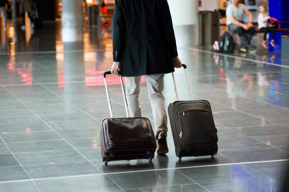 Man pulling two suitcases through an airport terminal.