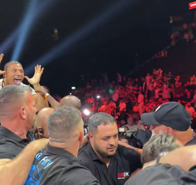 A man on someone's shoulders with his tongue out and hands up in a crowd.