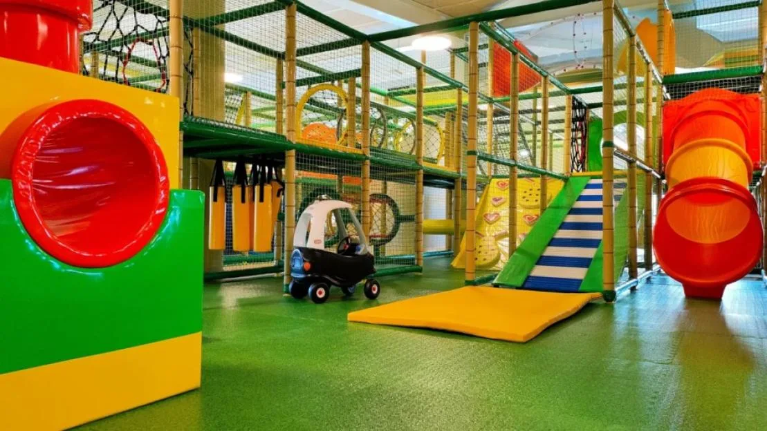 An indoor soft play center featuring a climbing frame, slide, toy car, and tunnel.